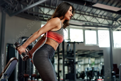 A fit sportswoman is doing exercises with dumbbells for chest and arms in a gym.