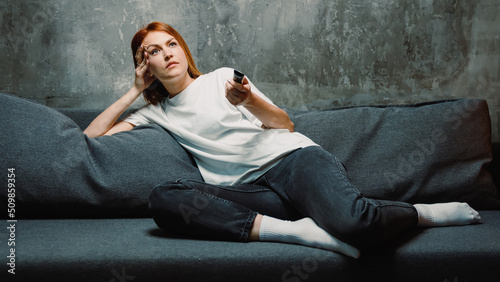 A young woman is bored and switches channels on the TV. Loneliness