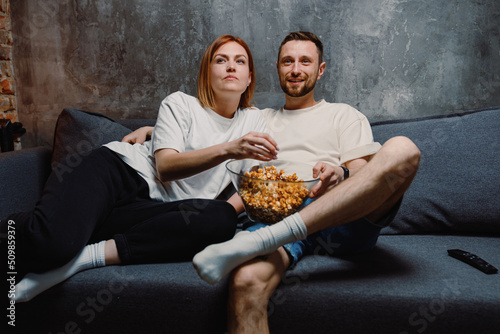 A couple in love eating popcorn are sitting at home. Evening movie viewing on TV
