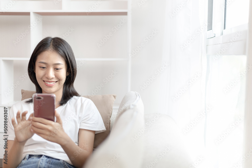 Asian woman sitting with smart phone on sofa in living room, Looking at tablet screen, Relaxing at home, Working through the Internet communication system, Happy working lifestyle. Asian woman sitting with smart phone on sofa in living room, Looking at tablet screen, Relaxing at home, Working through the Internet communication system, Happy working lifestyle.