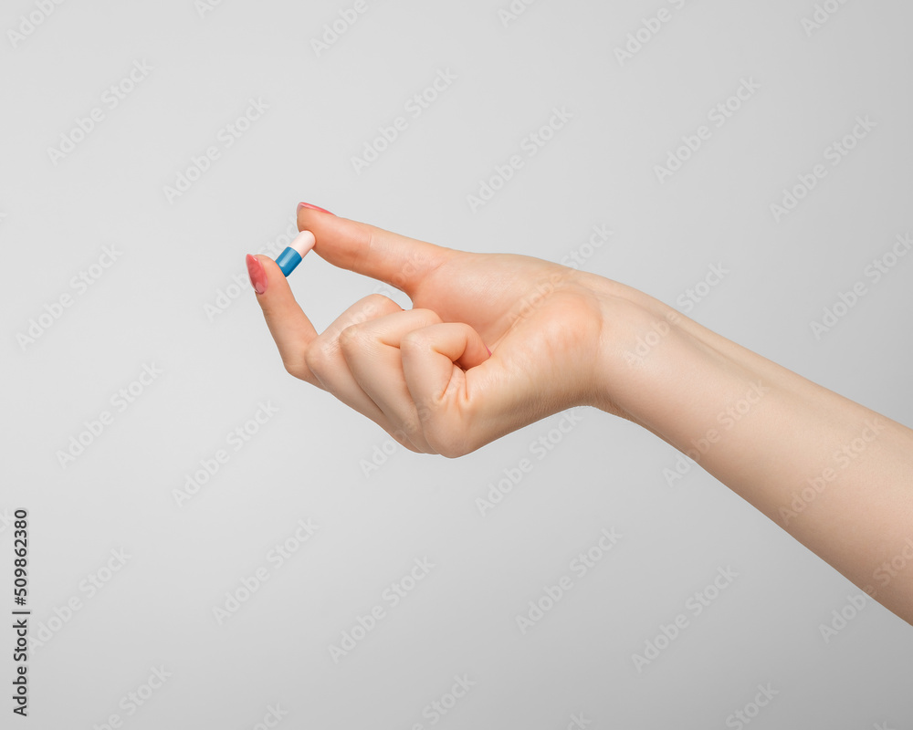 Tablet in a capsule in a woman's hand on gray background.