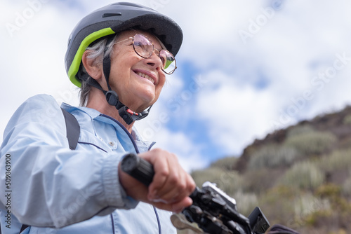 Portrait of smiling senior biker woman wearing sport helmet and eyeglasses in outdoors excursion with bicycle