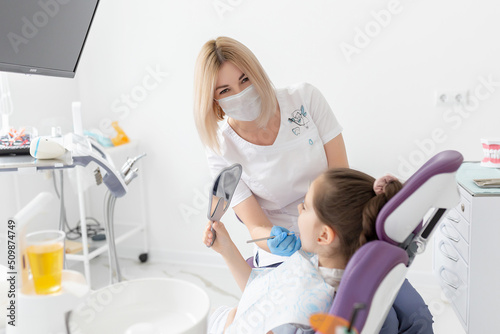 Child patient looking at her teeth through the mirror
