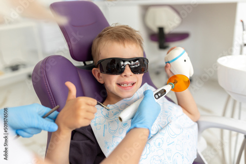 Dental clinic visit. Young positive boy patient showing thumbs up sign in dentist office