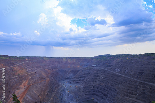 Open-pit iron ore mining. Drill rigs and excavators in the process. Heavy steel industry initial production chain. Thunderstorm clouds over the quarry.