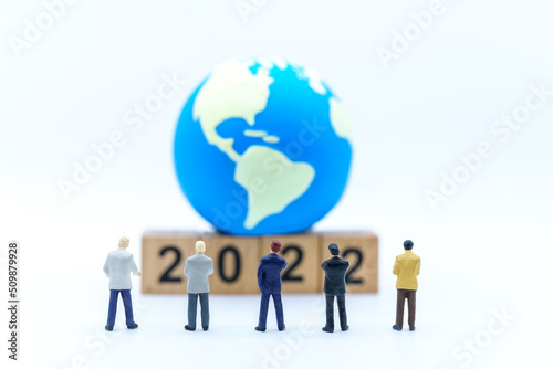 2022 New Year and Business Planning Concept. Closeup of group of businessman miniature figures standing and looking to wooden number block with mini world ball on white background.
