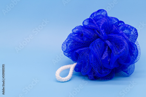 Blue mesh pouf bath sponge washcloth single object on blue background closeup photo with copy space. Soft synthetic shower wash cloth. Washing hygiene design element. Spa body care accessory product. photo