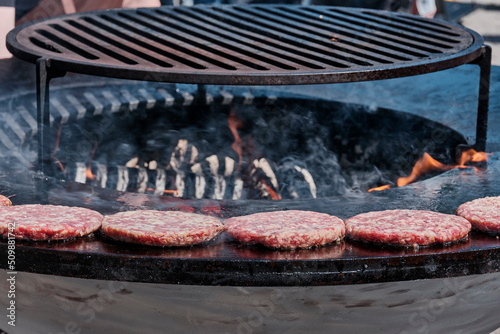 Raw burger patties are grilled on barbecue on open fire at park.