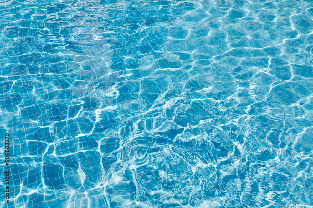 Clear water surface with ripple wave splashes and drops in swimming pool. Abstract turquoise or blue texture water wave and sunlight shadow reflections for background.