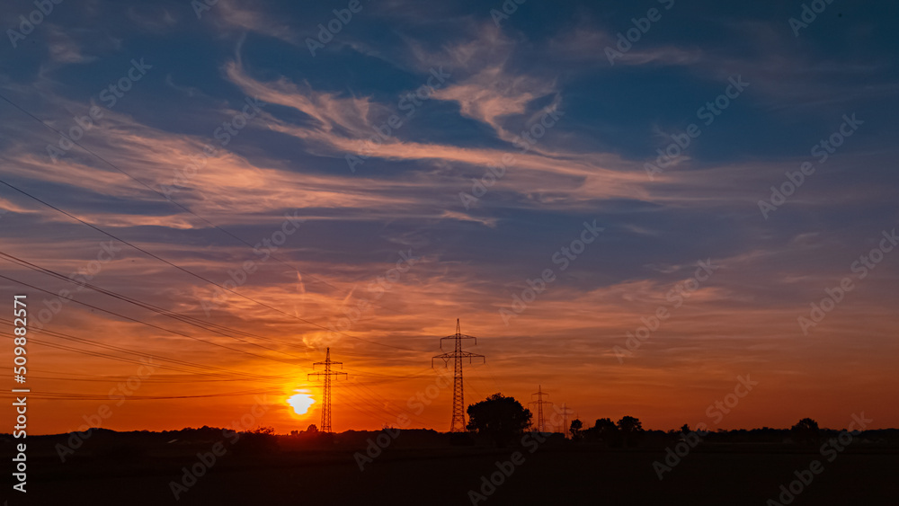 Beautiful sunset with a dramatic sky and overland high voltage lines near Tabertshausen, Bavaria, Germany Beautiful sunset with a dramatic sky and overland high voltage lines near Tabertshausen, Bavaria, Germany