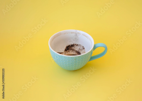 A blue cup with coffee grounds stands on a yellow background