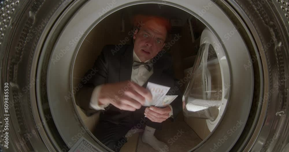 He throws dollar bills into the drum of the washing machine. Imitation of waste of money on utilities. Suit, white shirt, bow tie. Motivation to save. He throws dollar bills into the drum of the washing machine. Imitation of waste of money on utilities. Suit, white shirt, bow tie. Motivation to save.