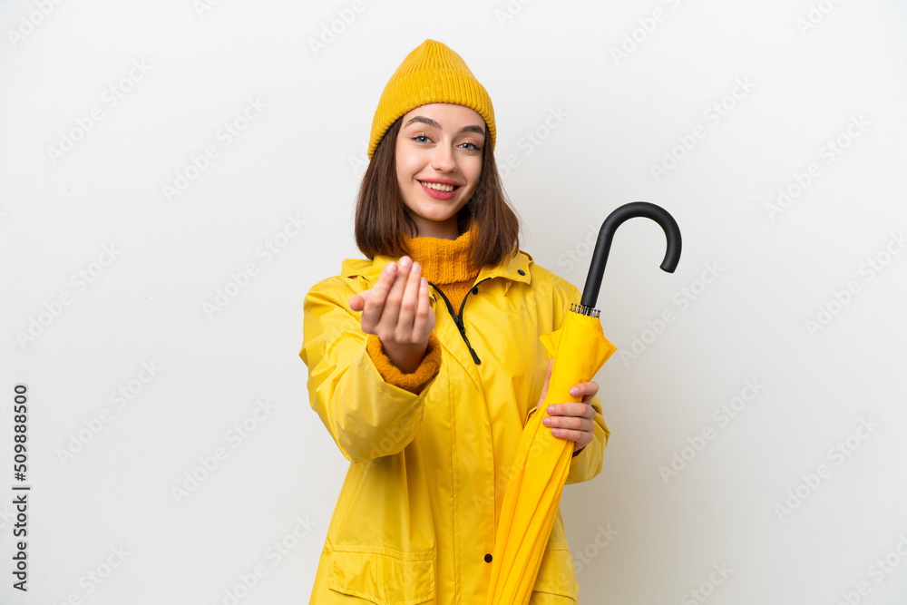 Young Ukrainian woman with rainproof coat and umbrella isolated on white background inviting to come with hand. Happy that you came
