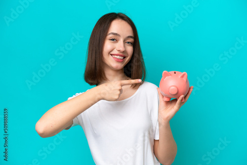 Young Ukrainian woman holding a piggybank isolated on blue background and pointing it