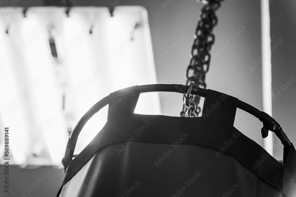 Punching bag on a chain in the karate hall. Black and white background retro image with film noise effect.