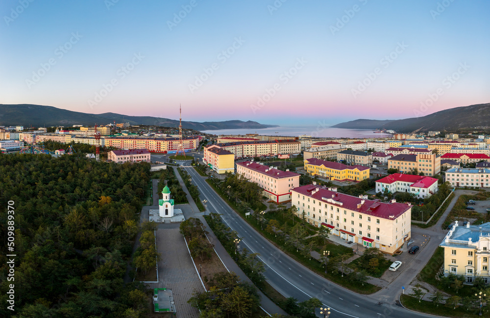 Fototapeta premium Aerial view of a northern seaside town. Top view of the streets, buildings and the chapel. In the distance the sea bay and mountains. Beautiful morning cityscape. Magadan city, Magadan Region, Russia.