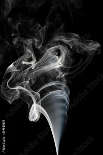 Puffs and curls of white smoke against a black background rising from a burning stick