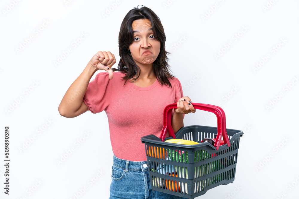 Young woman holding a shopping basket full of food showing thumb down with negative expression Young woman holding a shopping basket full of food showing thumb down with negative expression