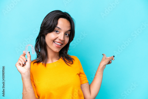 Young hispanic woman holding invisible braces isolated on blue background pointing back