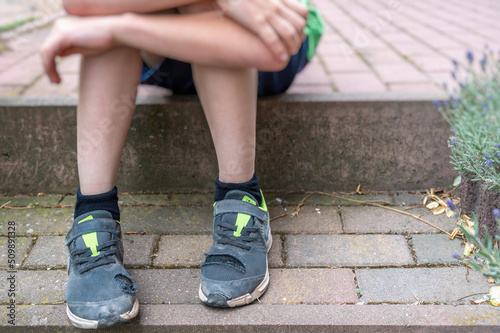 Kleiner Junge mit kaputten Schuhen als Symbol für Kinderarmut
