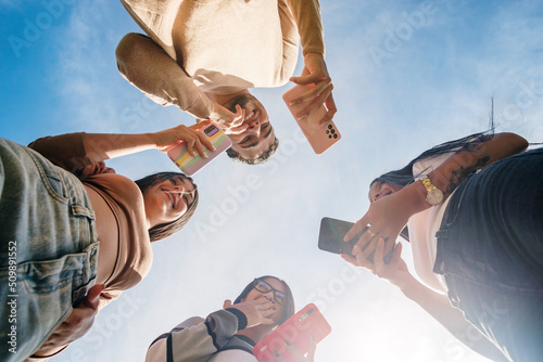 Group of friends smiling and using cell phone in a sunny day background