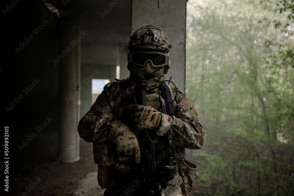 Military soldier in uniform standing with a weapon in his hands at night. Dark portrait of a military man