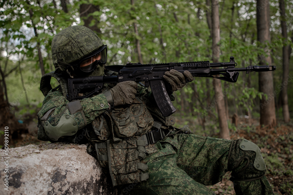 Russian military soldier in uniform sitting in the forest, firing a weapon