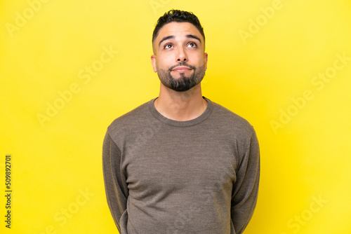 Leinwand Poster Young Arab handsome man isolated on yellow background and looking up