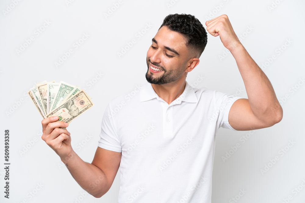 Young Arab man taking a lot of money isolated on white background celebrating a victory Young Arab man taking a lot of money isolated on white background celebrating a victory