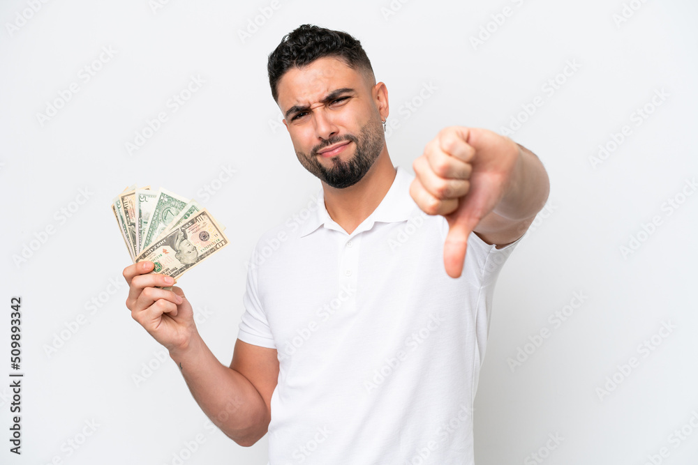 Young Arab man taking a lot of money isolated on white background showing thumb down with negative expression Young Arab man taking a lot of money isolated on white background showing thumb down with negative expression