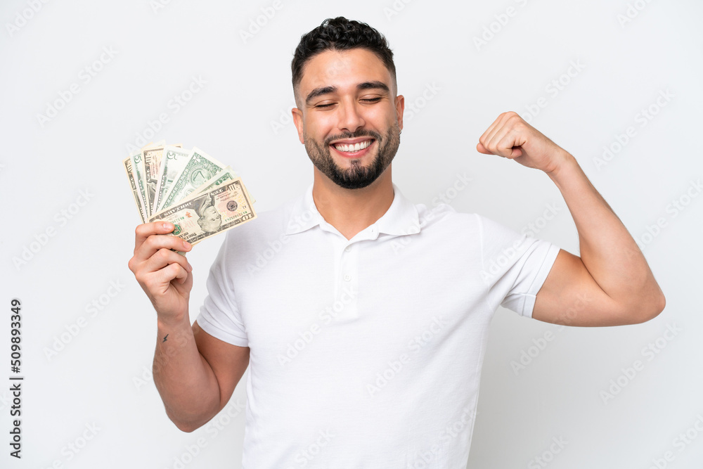 Young Arab man taking a lot of money isolated on white background doing strong gesture Young Arab man taking a lot of money isolated on white background doing strong gesture