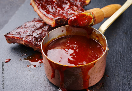 Hot and spicy barbecue sauce in a casserole as close-up with spare ribs in background photo