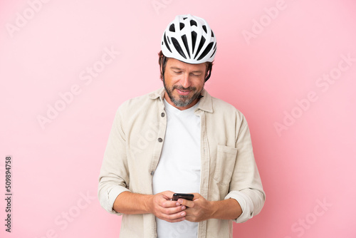 Senior dutch man with bike helmet isolated on pink background sending a message with the mobile © luismolinero