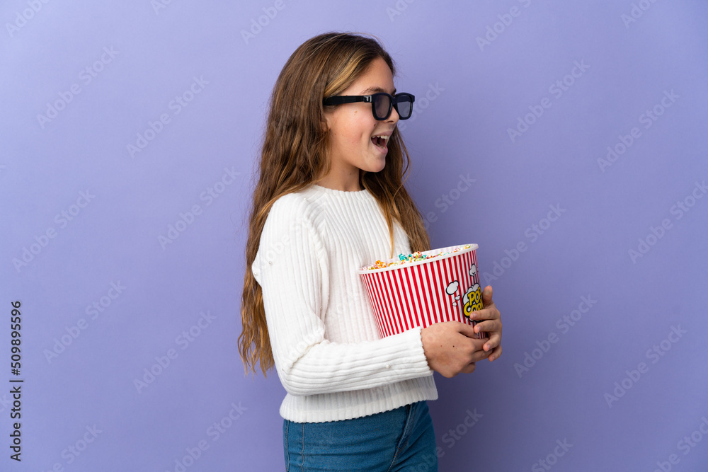 Child over isolated purple background with 3d glasses and holding a big bucket of popcorns Child over isolated purple background with 3d glasses and holding a big bucket of popcorns