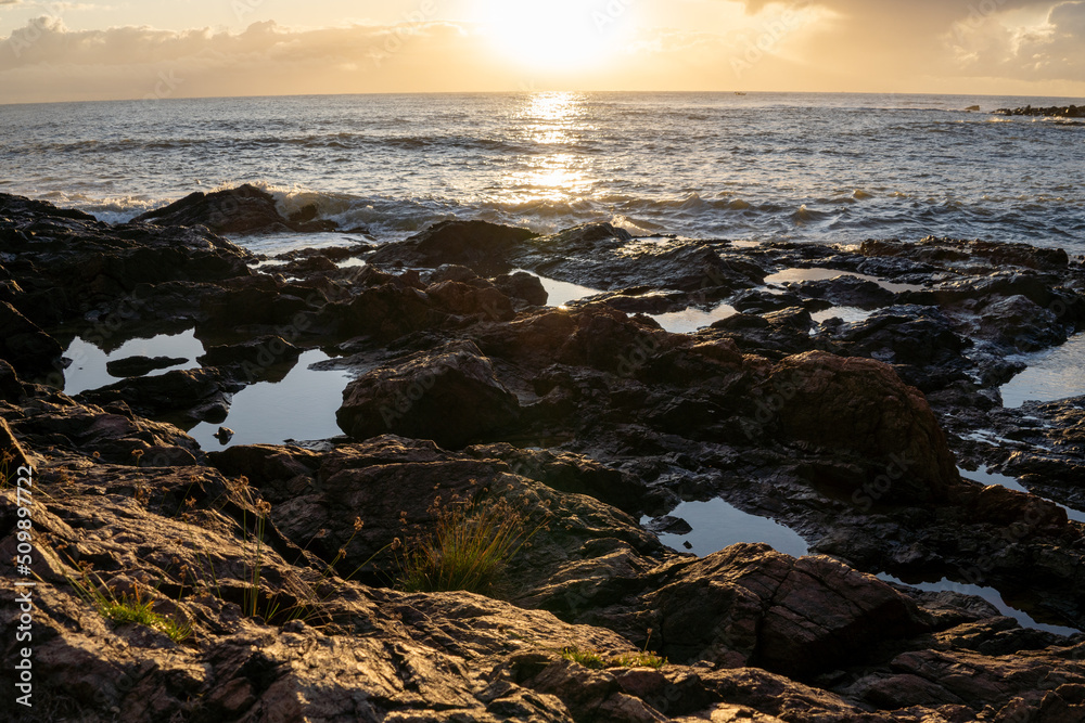 Obraz premium Sun rising on the sea horizon behind rocks on the beach