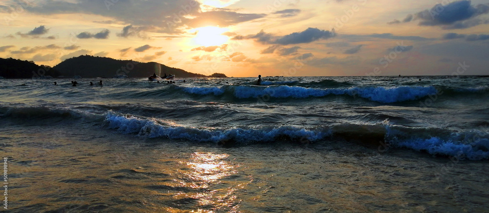 Coast with waves in the sea at sunset. Unrecognizable people bathe in the waves during sunset.