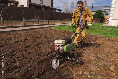 Farmer cultivates the ground soil in the garden using a motor cultivator or tiller tractor. Modern farming and technology agriculture.  photo