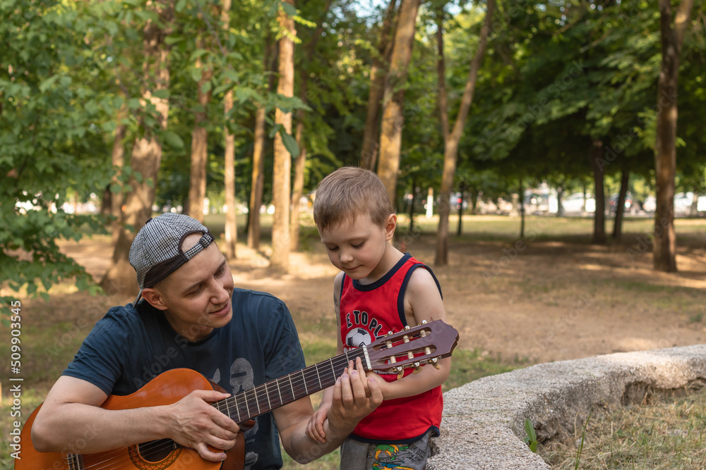 father teaching his son to play the guitar outside