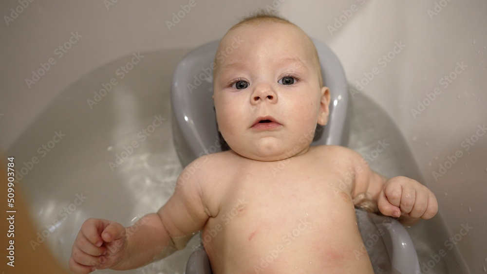 Portrait of an adorable cute baby taking his first bath and smiling. Bathing a newborn in a tub. First days of life. A little boy takes a bath for the first time. Portrait of an adorable cute baby taking his first bath and smiling. Bathing a newborn in a tub. First days of life. A little boy takes a bath for the first time.