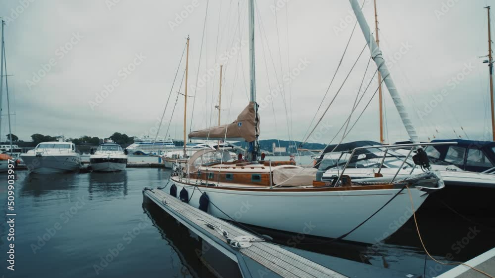 Blue sailboat moored to a pier in yacht marina at sunset. Colorful cloudscape, reflections on the water. Sailing, recreation theme. Blue sailboat moored to a pier in yacht marina at sunset. Colorful cloudscape, reflections on the water. Sailing, recreation theme.