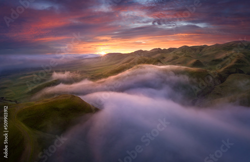 Dramatic sunrise above patchy fog in rolling hills, Central California, USA