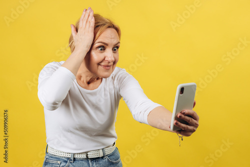 Gorgeous mature woman with a phone in her hand surprised by what she saw on the screen on a yellow background