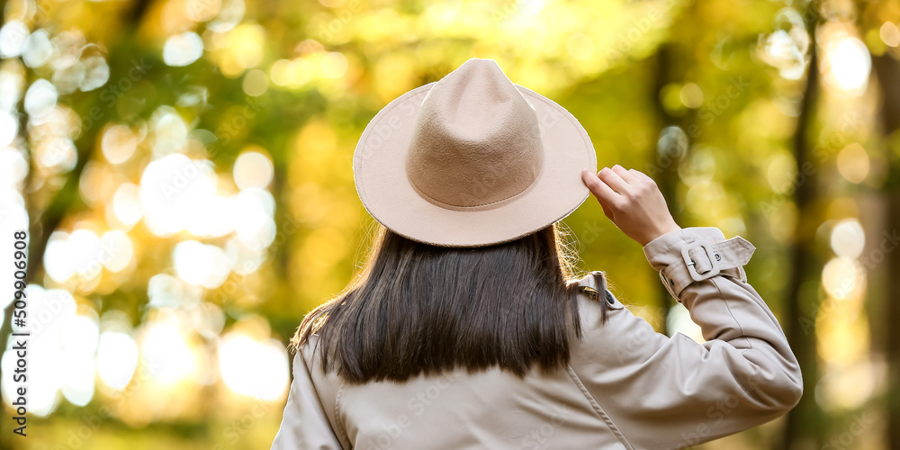 Pretty young woman wearing hat and coat while walking in autumn park, back view