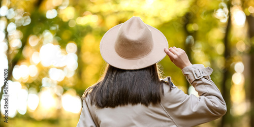 Pretty young woman wearing hat and coat while walking in autumn park  back view