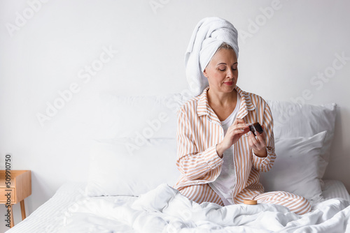 Skincare routine and healthy aging, mature woman applying face cream in bed w...