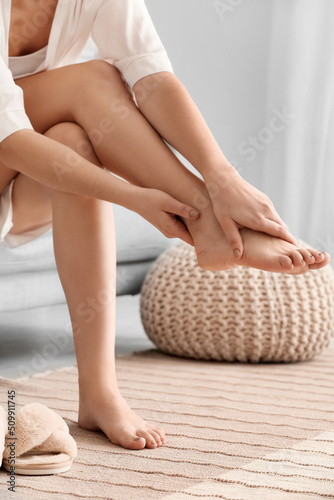 Woman sitting on sofa and making foot massage in room, closeup © Pixel-Shot