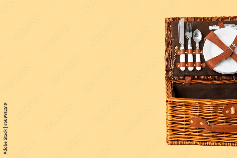 Wicker basket with tableware for picnic on beige background