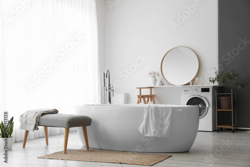 Interior of light room with soft bench  bathtub and washing machine
