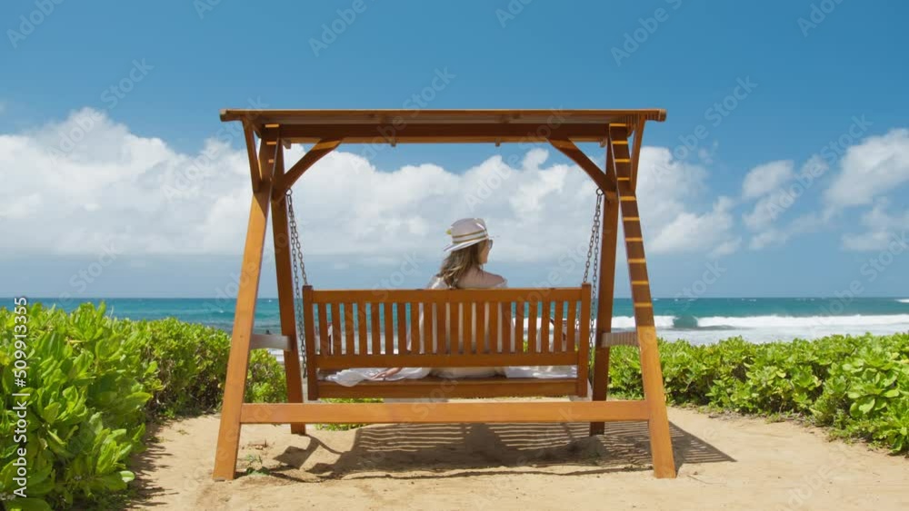 Back view young relaxed woman enjoying summer vacation, swaying sitting on swings with ocean beach view. Serene incredible summer rest, paradise dream. Beautiful resort outdoors happiness freedom feel Back view young relaxed woman enjoying summer vacation, swaying sitting on swings with ocean beach view. Serene incredible summer rest, paradise dream. Beautiful resort outdoors happiness freedom feel