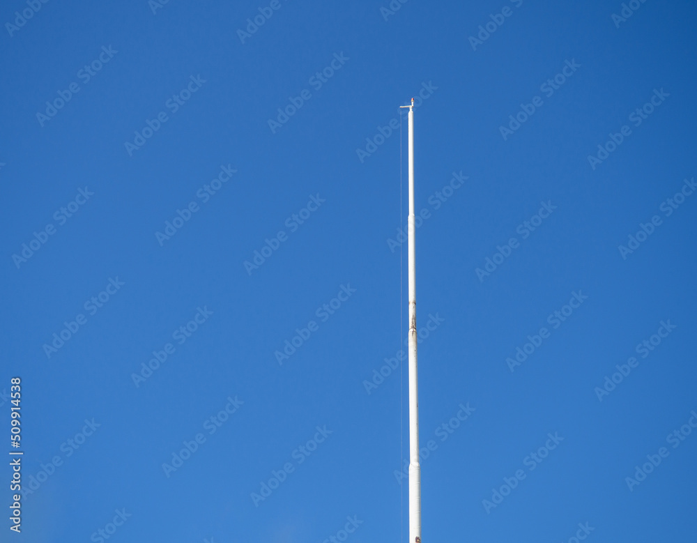 Empty white flagpole against the blue sky. Lowered flag. - obrazy, fototapety, plakaty 